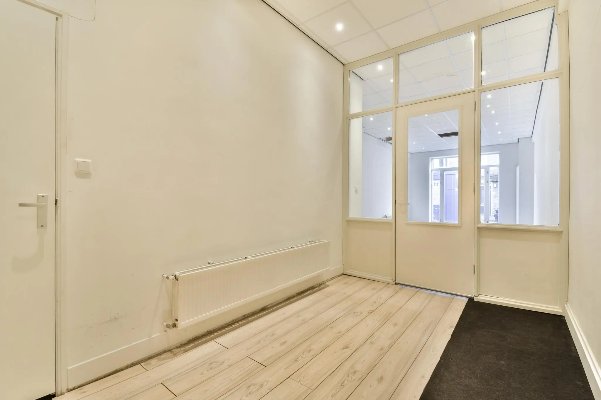 Lichte hal met houten vloer, radiator en glazen tussenwand in een pand aan de Korte Schimmelstraat.